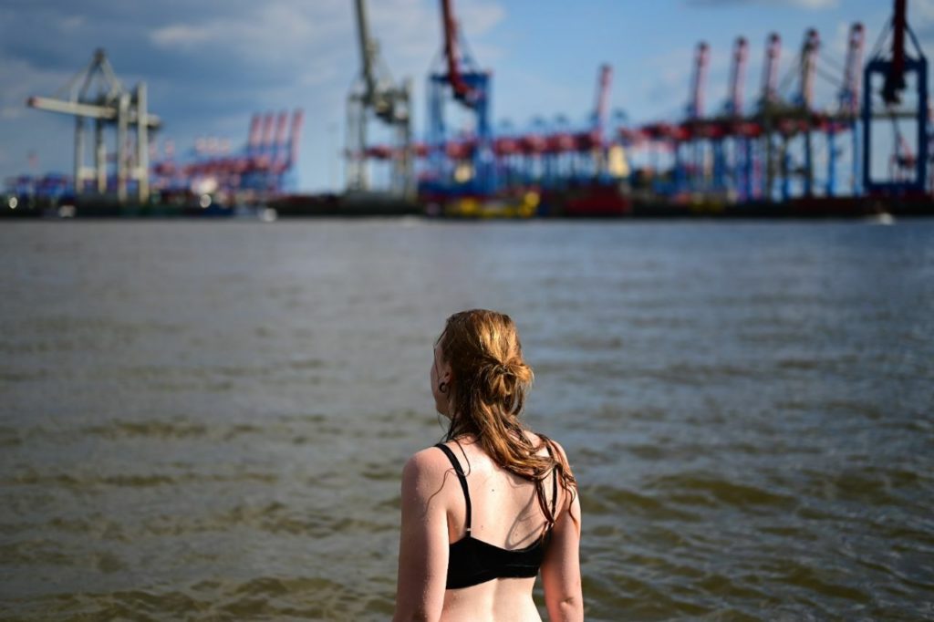 Anna steht am Elbstrand im Wasser und schaut auf die Kräne des Hamburger Hafens